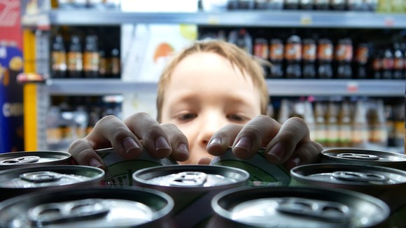 A young person taking a can of soda from a shelf in a store beverage aisle.