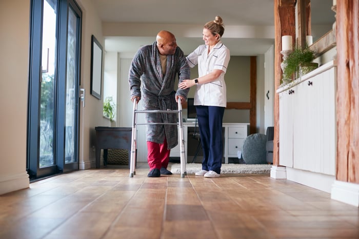 A person helping another person using a walker.
