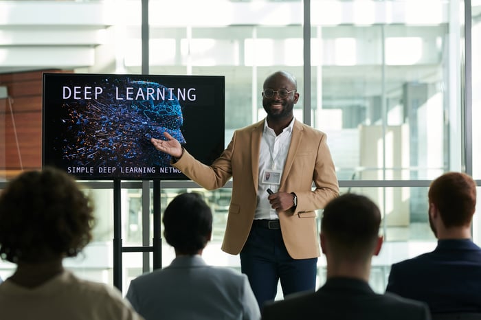 Person in front of audience, gesturing to a display that reads "Deep Learning."