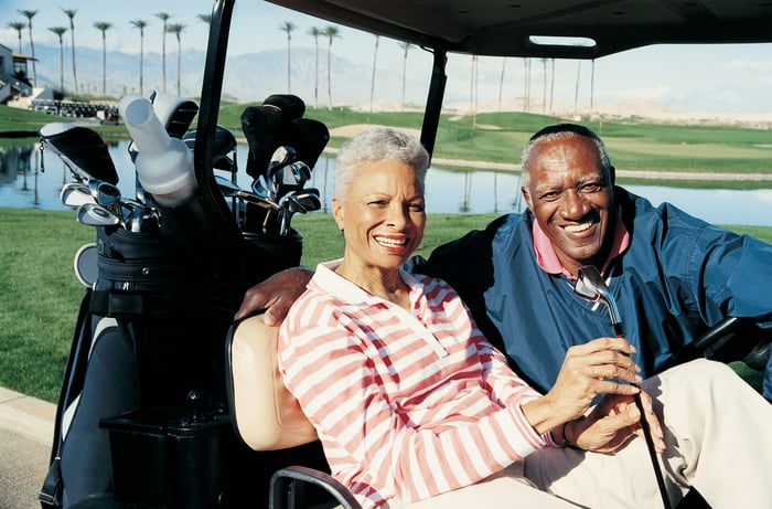 Two people sitting in a golf cart at the golf course.
