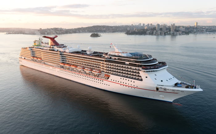 A cruise ship in open water with a city's tall buildings in the background.