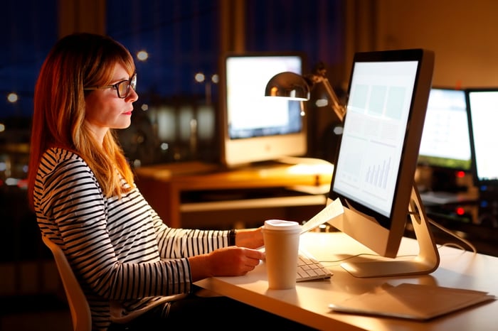 Person sitting at office desk, looking at computer monitor.