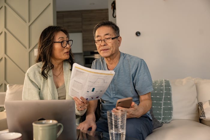 A couple sit on the sofa looking at a laptop and the financial news.