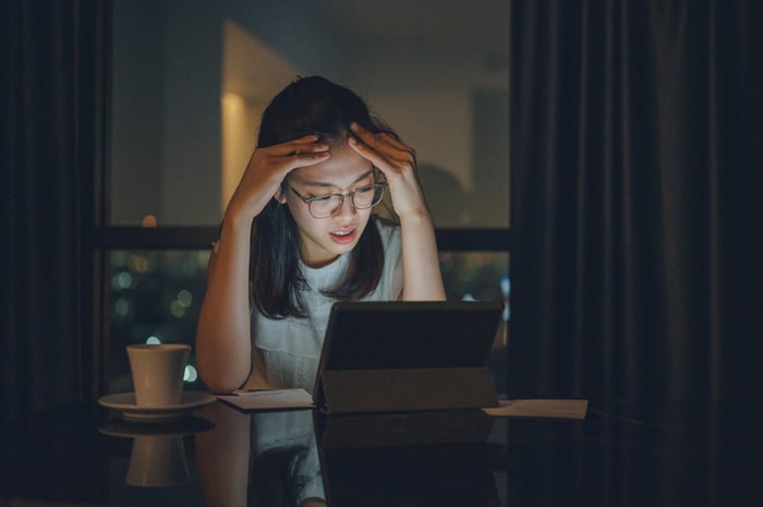 Concerned young person with head in hands gazing at a screen.