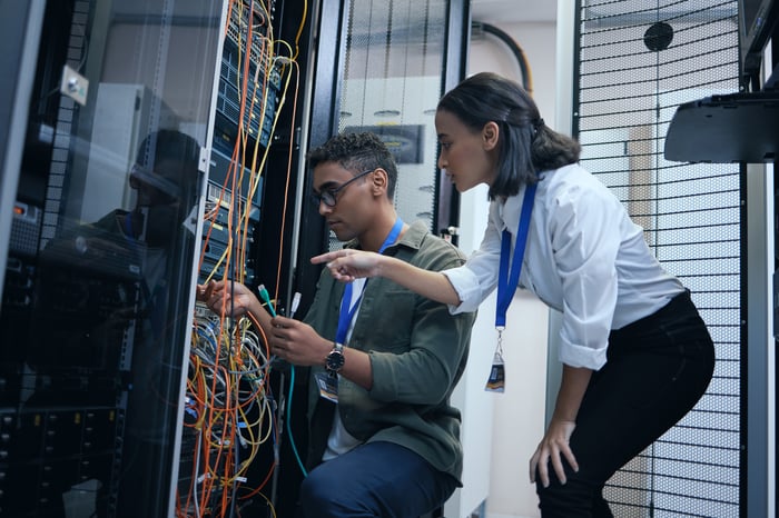 Two engineers checking wires and switches for an enterprise data center server tower.