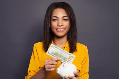 22_03_07 A person putting a 100 dollar bill into a piggy bank _GettyImages-1203959263