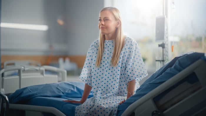 Healthy-looking patient sitting on edge of hospital bed. 