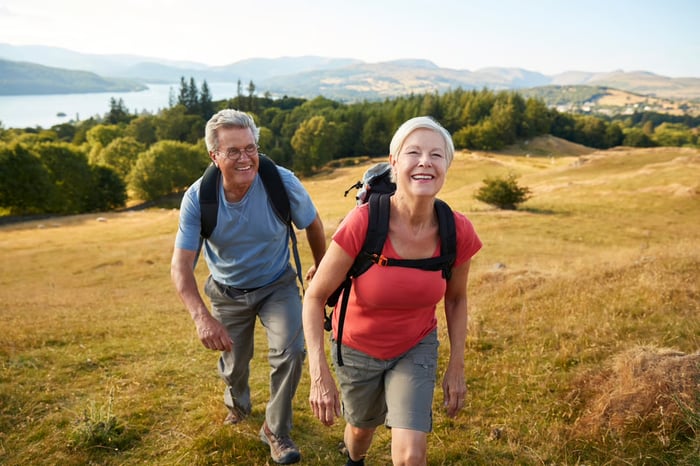 A couple hiking up a grassy hill with a fjord in the background. 
