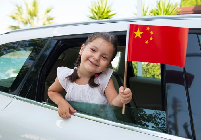 Little girl waving a Chinese flag out of a car window.