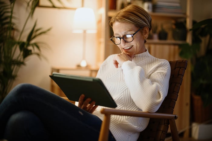 A person smiles while sitting in a chair and looking at a tablet.