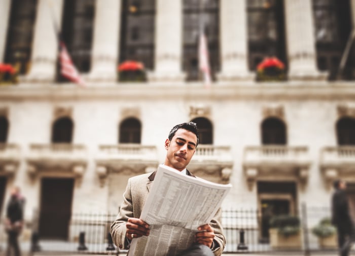 Trader reading newspaper in front of New York Stock Exchange.