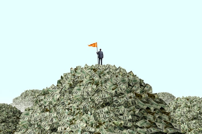 Person with flag, standing on a giant pile of cash.