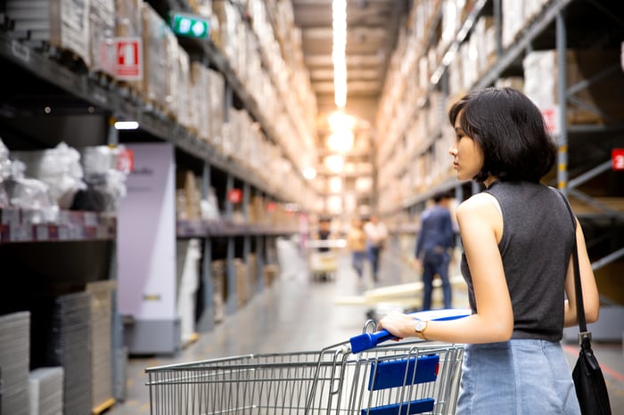shopper pushing cart in aisle of warehouse store.