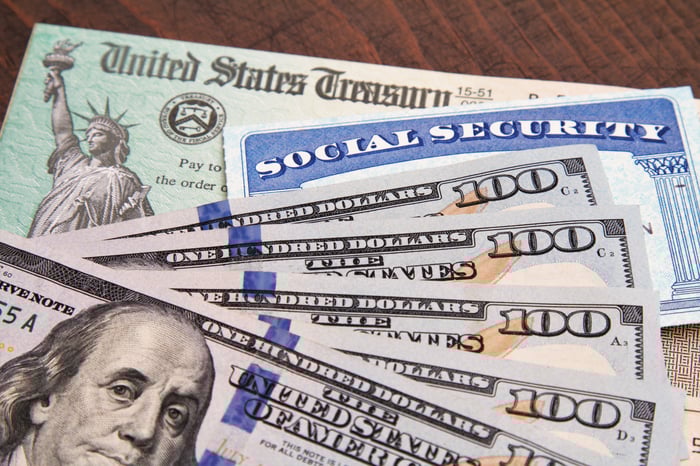 U.S. currency, a Social Security card, and U.S. Treasury check sit on a wooden surface.