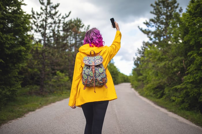 A person holding up a cell phone for signal on a country road.