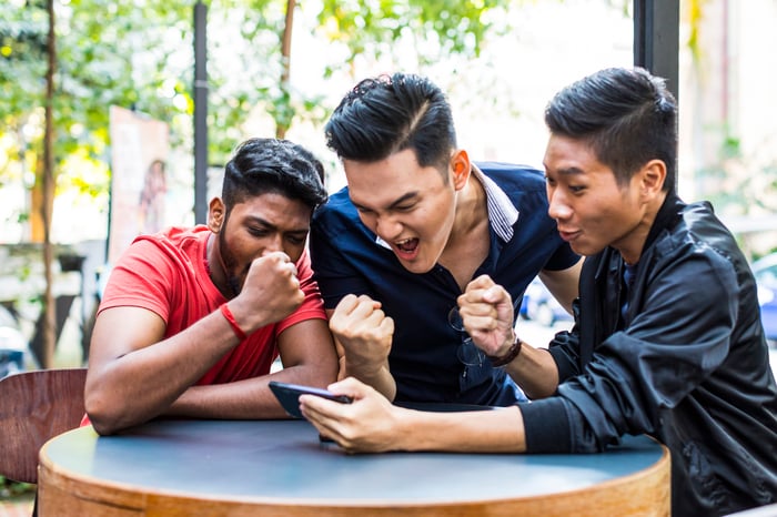 Three people pump their fists while looking at a smartphone.