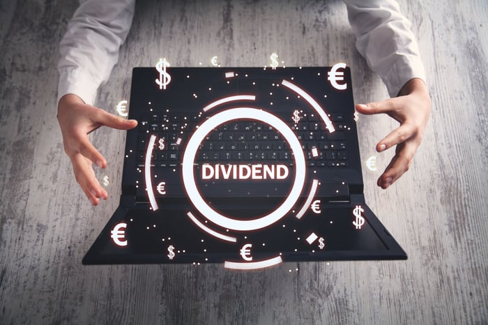 Hands near a laptop with "Dividend" and currency symbols above it.