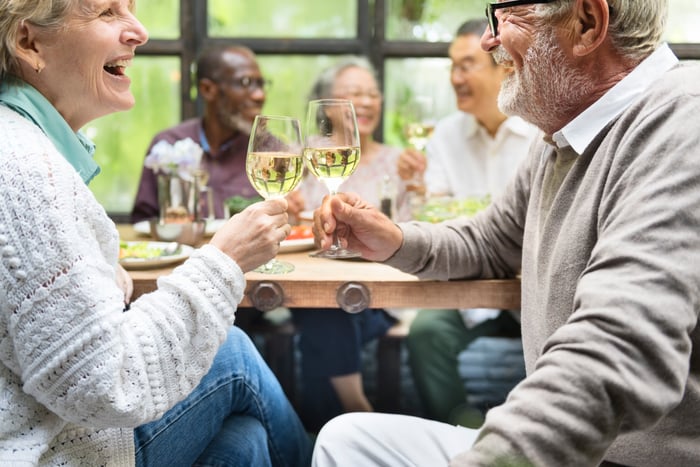 People toasting with wine glasses as others chat in the background. 