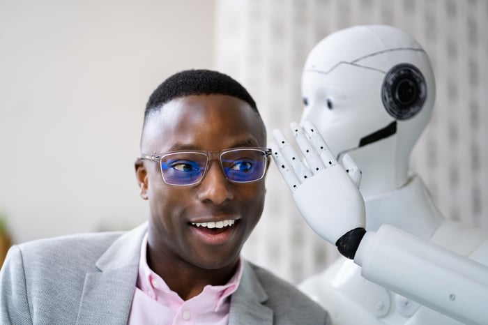 A humanoid robot whispers secrets to a smiling human.