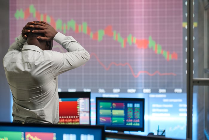 A distressed trader watching a falling stock price chart on a big screen.