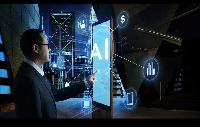 A person pointing to a display with a digital image of "AI" and other icons surrounding the display.