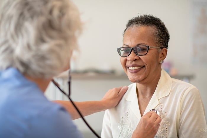 A person smiles while a health professional uses a stethoscope to examine them.