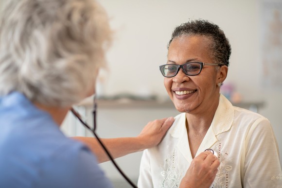 A person smiles while a health professional uses a stethoscope to examine them.