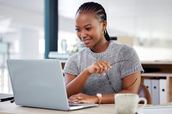 A smiling person looking at a laptop.