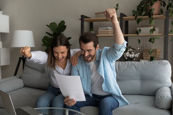 Two people looking at a document on a couch and cheering.