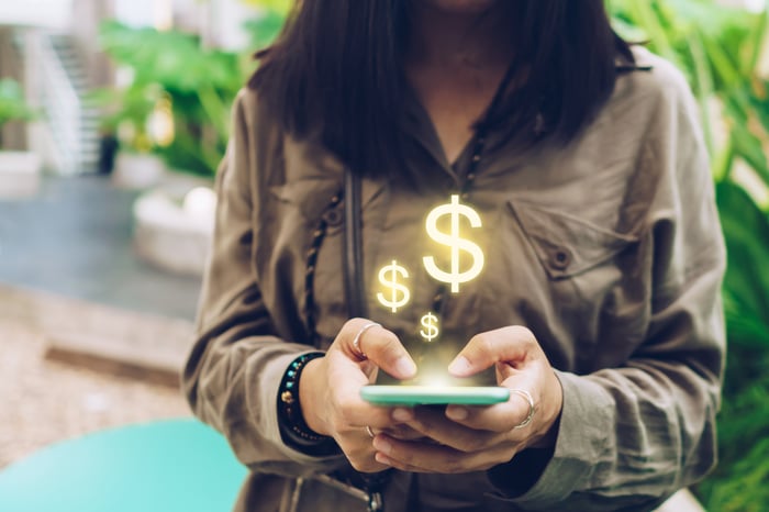 Person using phone with dollar signs floating above it.