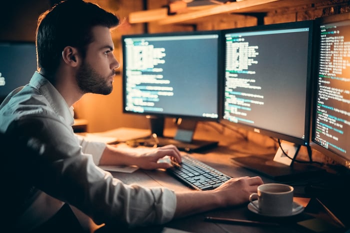 A person reviewing software code on several computer screens.
