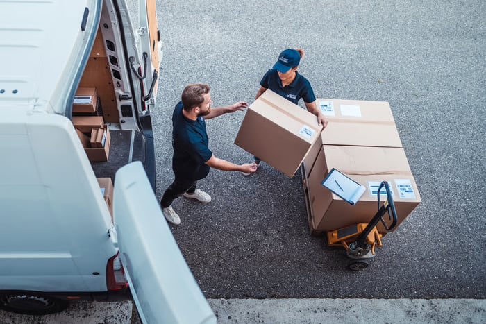 Two people loading packages into a moving van. 