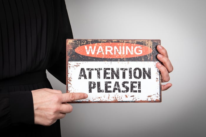 A person holding a sign that says Warning, Attention Please.