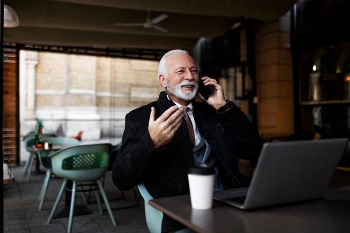 Someone sitting at a restaurant table in front of a laptop while talking on the phone.