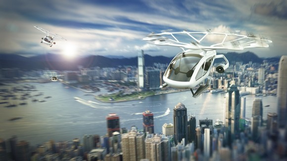 An air taxi flying over a city by a river.