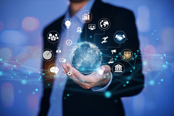 Person in suit holds a virtual earth with symbols depicting ideas, buildings, connections, and more.