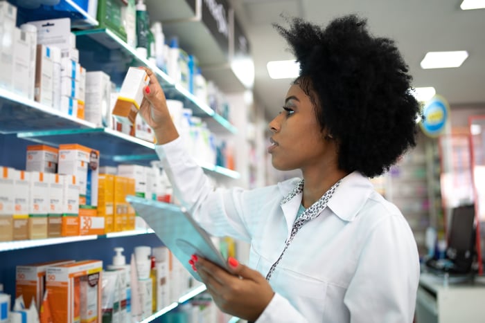 Person checking medicine on a shelf in a pharmacy.