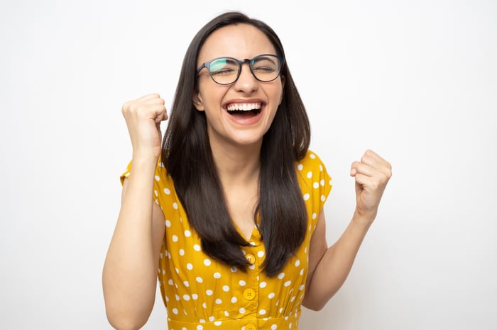A person in a yellow dress is smiling and pumping their fists in excitement.
