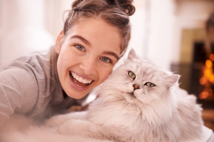 Someone is smiling with her head next to a fluffy cat.
