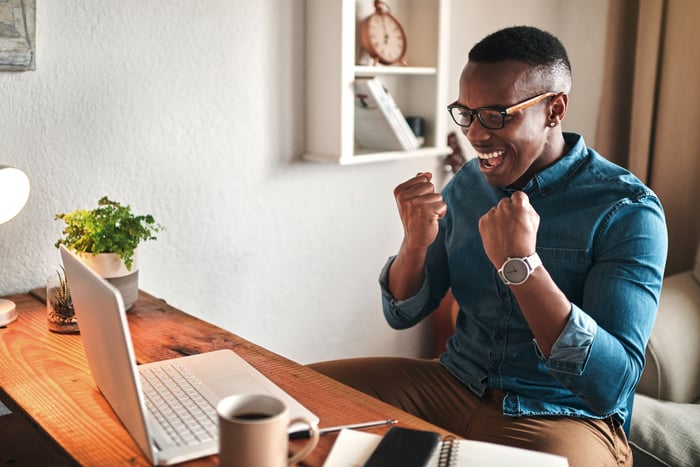A person celebrates while looking at a laptop.