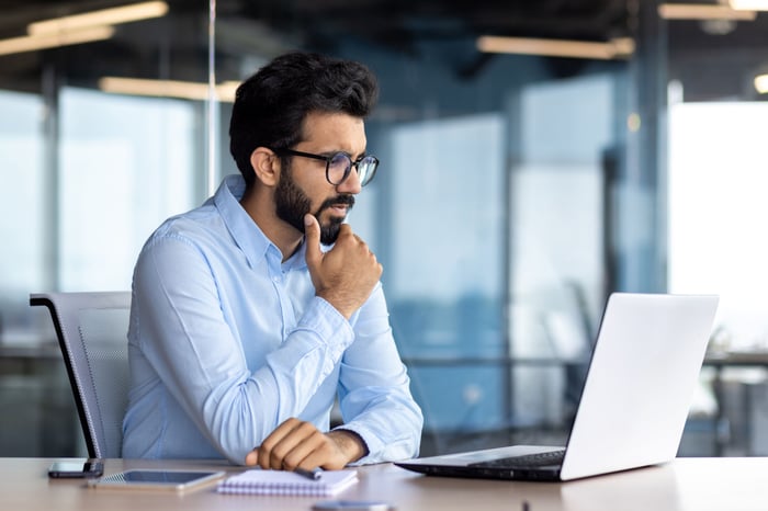 A person sitting in front of a laptop computer, looking thoughtful.