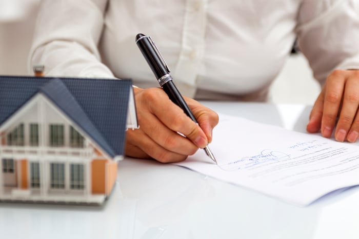 Hand writing on a document next to a model of a house. 
