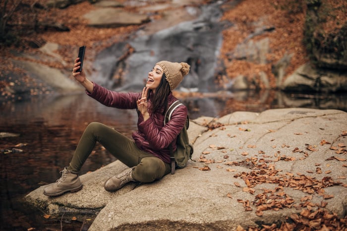 A person takes a selfie with a smartphone in a forest.