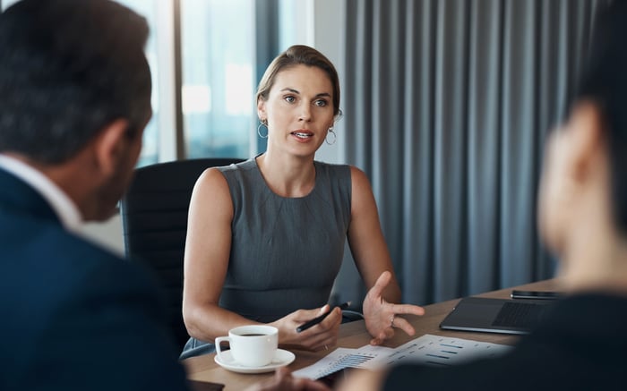 Three people discussing graphs on sheets of paper in a meeting room.