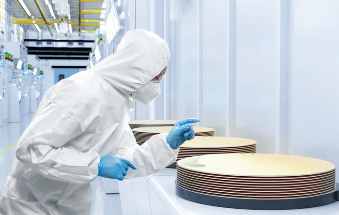 A technician in clearn room suit looks at a stack of wafers. 