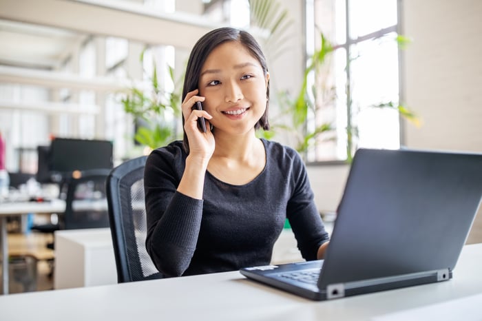Someone is on the phone, smiling, in front of an open laptop.