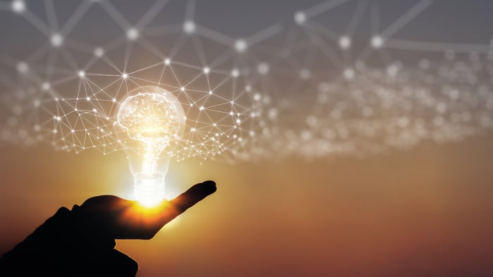 A hand holding a glowing light bulb beneath a net of interconnected white nodes.