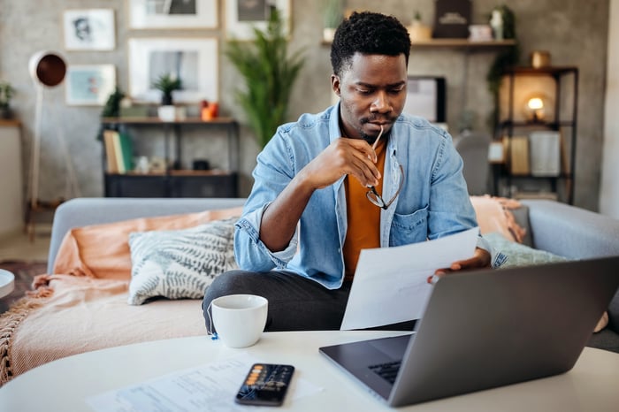 Person with a neutral expression sitting on a couch and looking at documents.