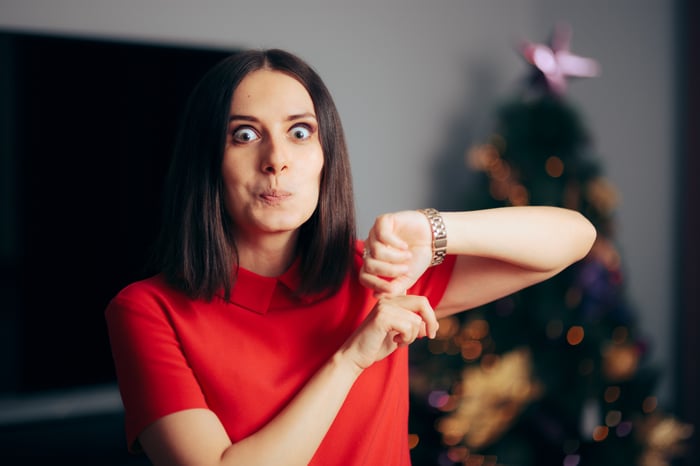 Person checking watch near Christmas tree.