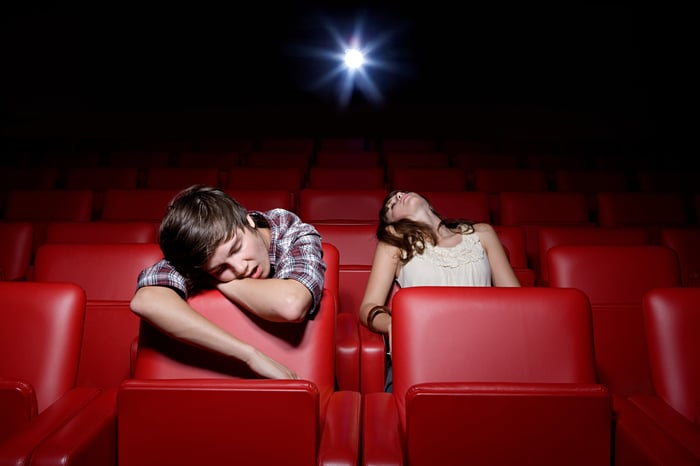 Two people asleep at a movie theater as the projector plays.